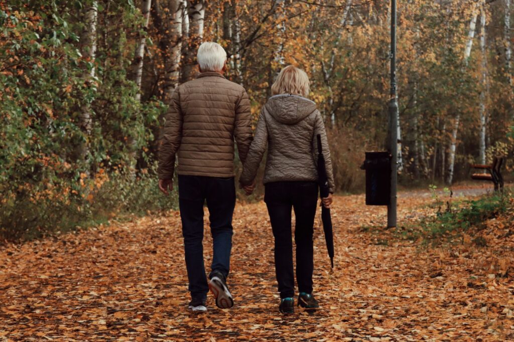 Un couple âgé marche côte à côte sur un sentier couvert de feuilles mortes